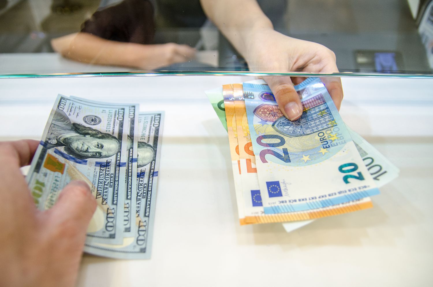 Hands exchanging US dollars and Euros through a glass counter.